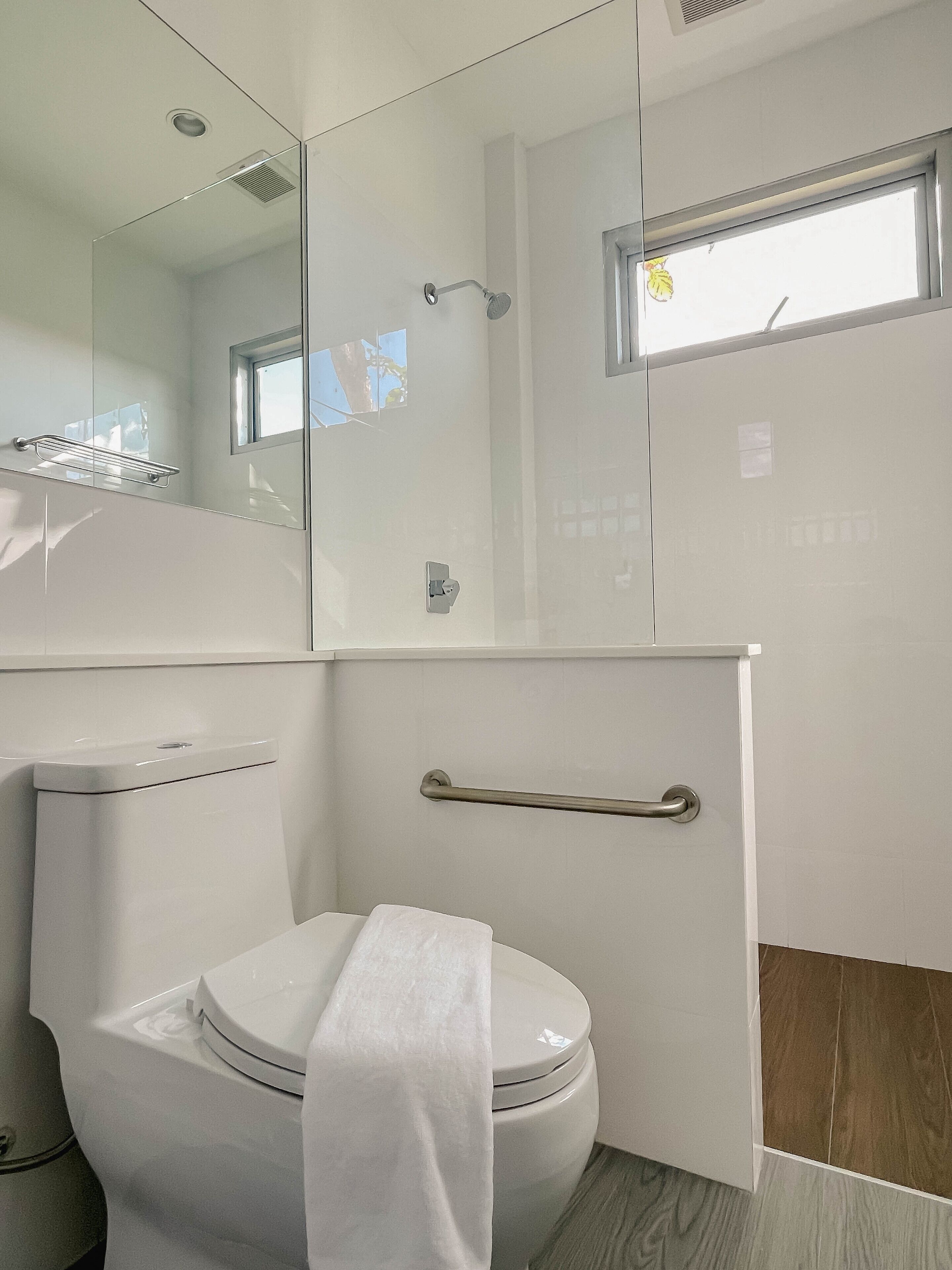 A modern bathroom with a toilet, a shower, and a glass-enclosed vanity.