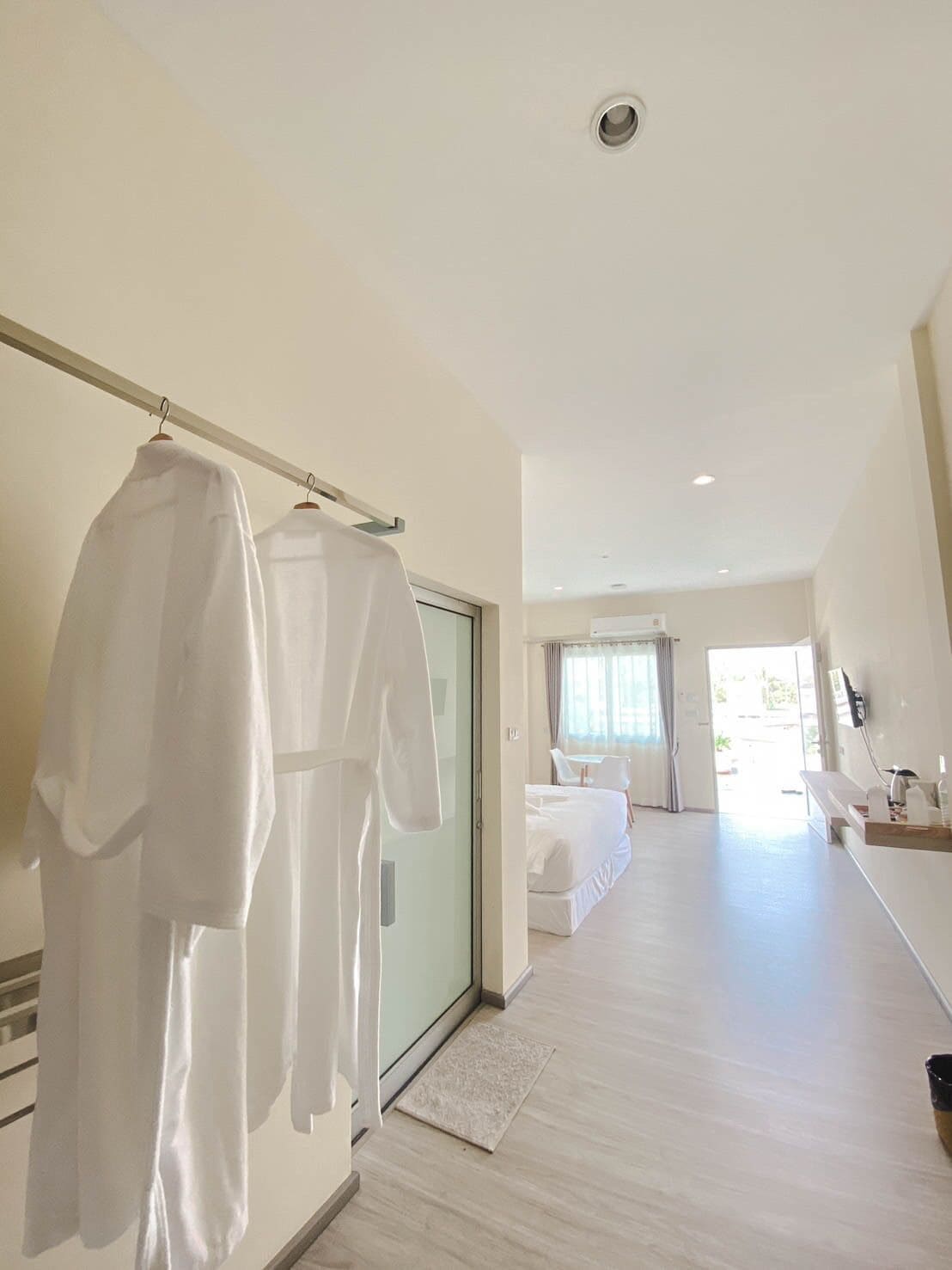 Una habitación de hotel moderna con una cama grande, una zona de estar con sofá y mesa, y un baño con espejo y lavamanos.