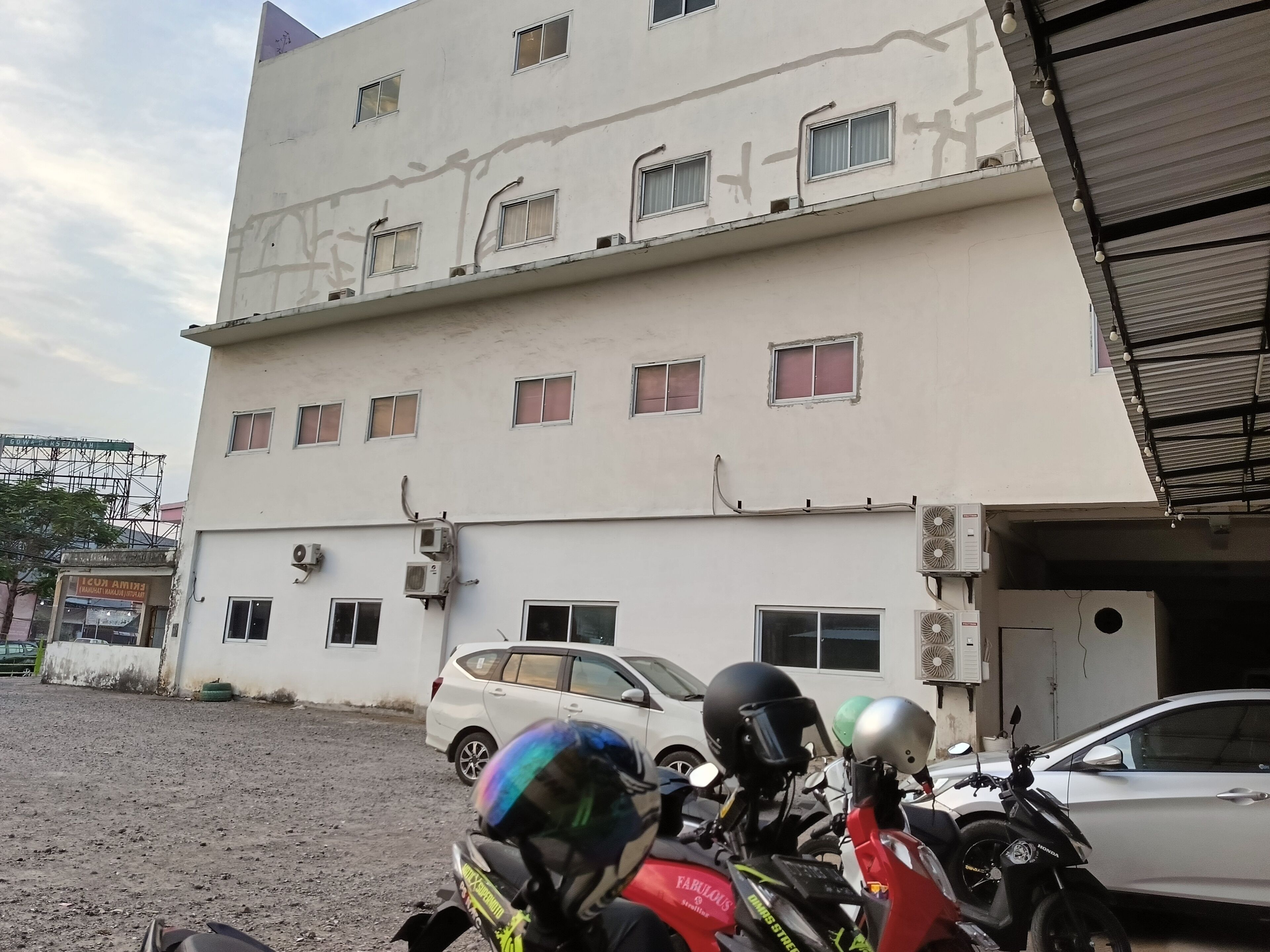 Un immeuble à plusieurs étages, doté de plusieurs unités de climatisation, avec une voiture garée et une moto avec des casques.