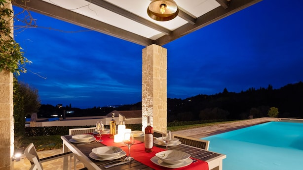 Un espace extérieur aménagé pour les repas, avec une piscine, un pilier en pierre et une vue sur le paysage.