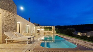 Un bâtiment en pierre doté d’une piscine, de chaises longues et d’un espace patio.