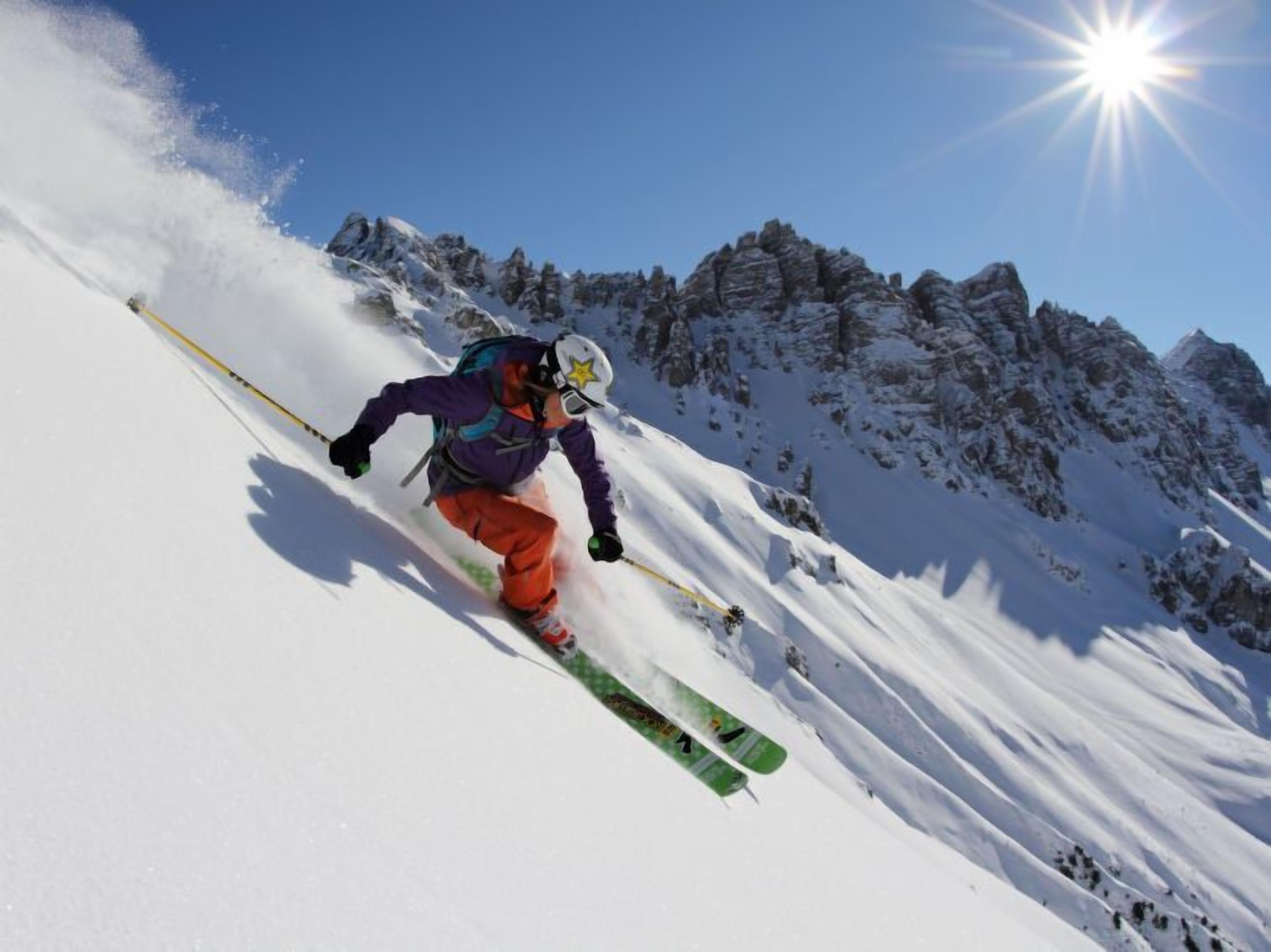 A skier on a snowy slope with a clear sky and sun.