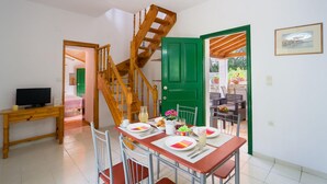 Un coin repas avec un escalier en bois, une porte verte et une table dressée pour deux personnes, avec des assiettes, des couverts et une carafe de limonade.