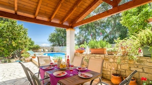 Une terrasse extérieure dotée d’une pergola en bois, d’un revêtement de sol en pierre et d’une piscine en arrière-plan.