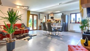 Una sala moderna con un sofá rojo, una zona de comedor con una mesa y sillas, una cocina al fondo y una planta grande en maceta al frente.