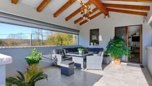 Un patio cubierto con techo de madera, mobiliario exterior, plantas en macetas y vistas al exterior.