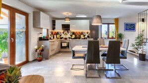 Una cocina moderna con zona de comedor, que incluye una isla grande, iluminación colgante y vistas al exterior.
