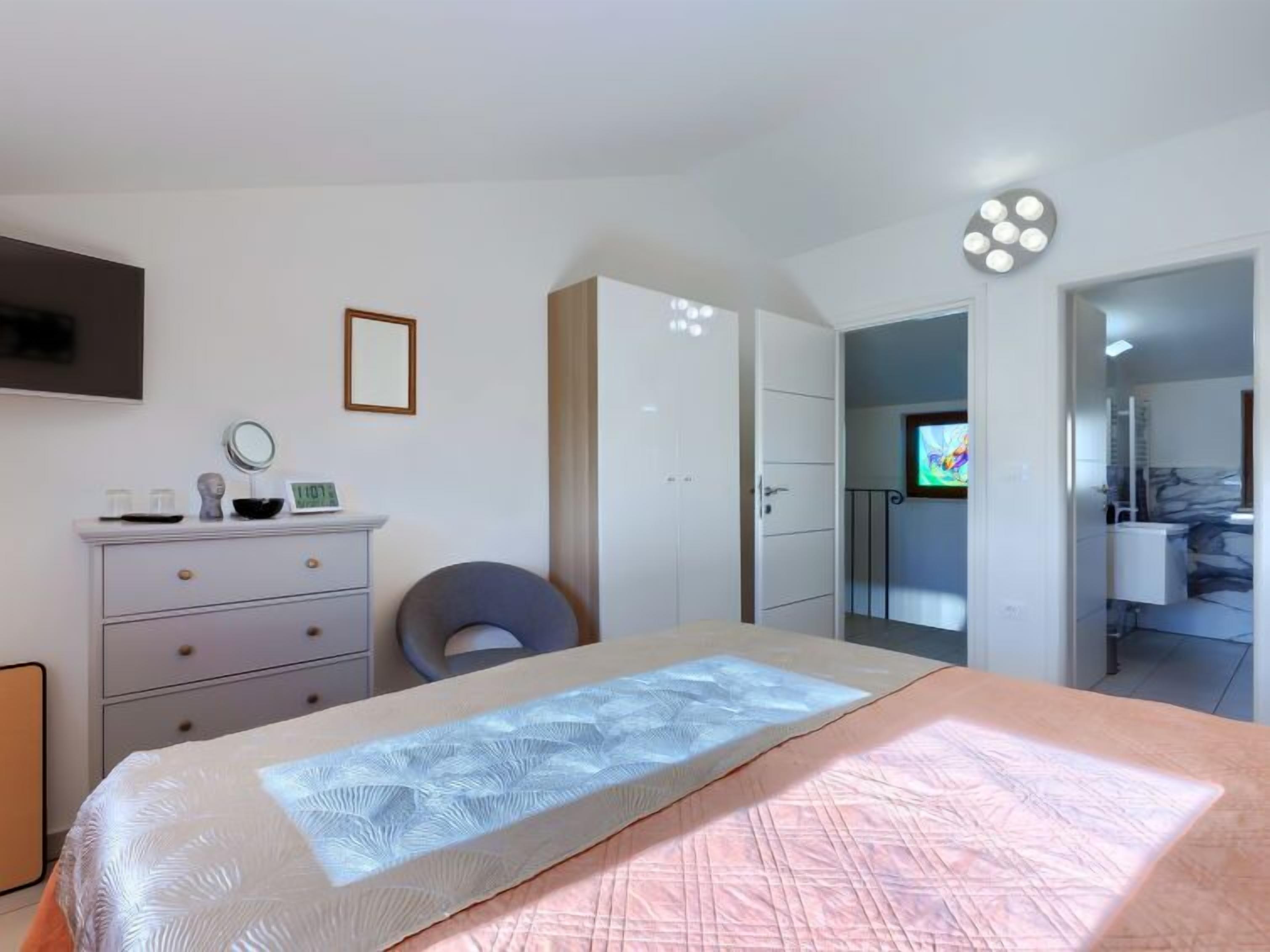 Ein Schlafzimmer mit Bett, Kommode, Stuhl, Fernseher und angrenzendem Badezimmer.