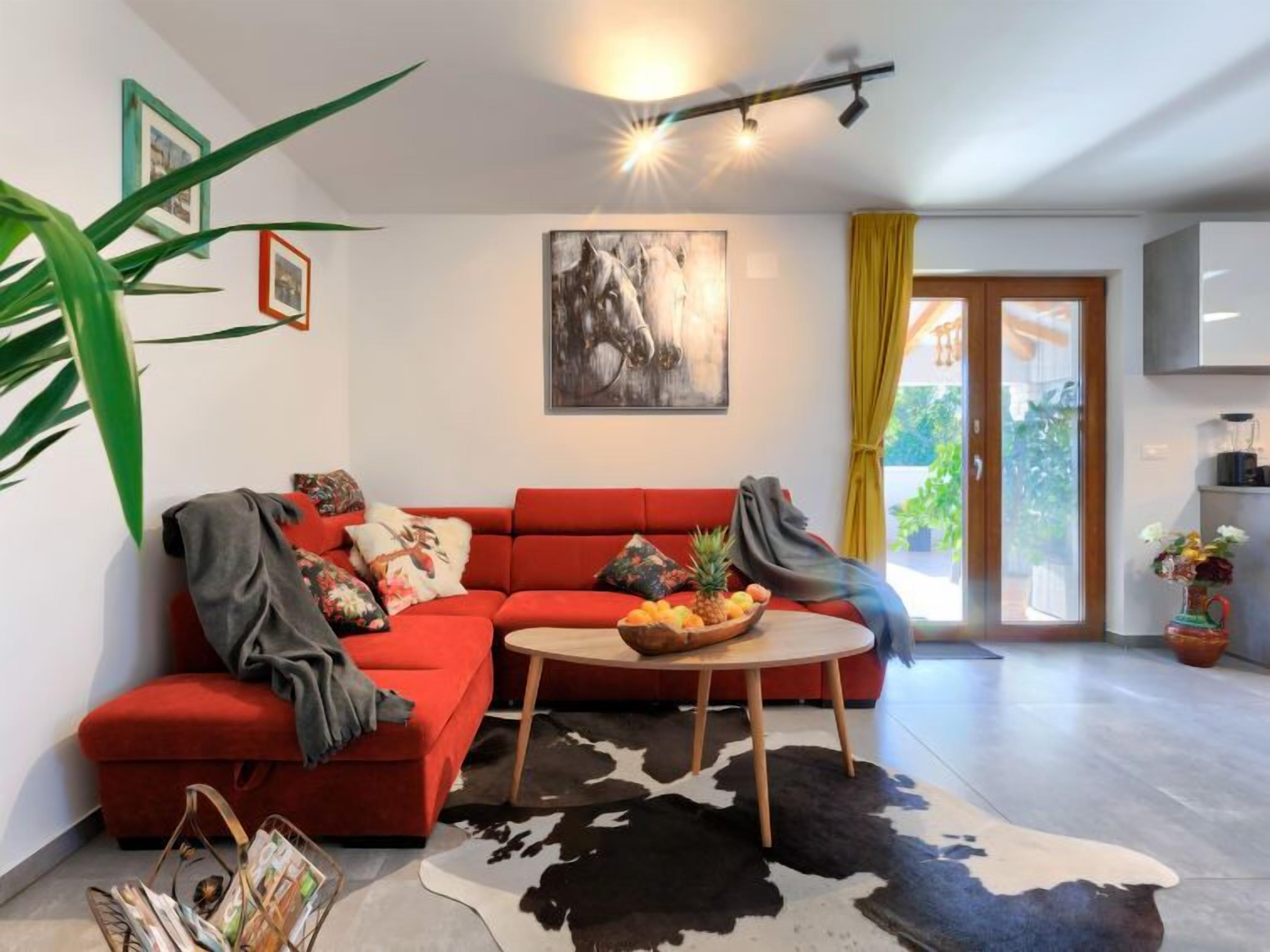 A modern living room with a red sofa, a round coffee table, and a cowhide rug. There is a painting on the wall and a plant in the corner.