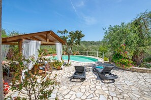 A stone patio with a pool, wooden pergola, and lounge chairs.