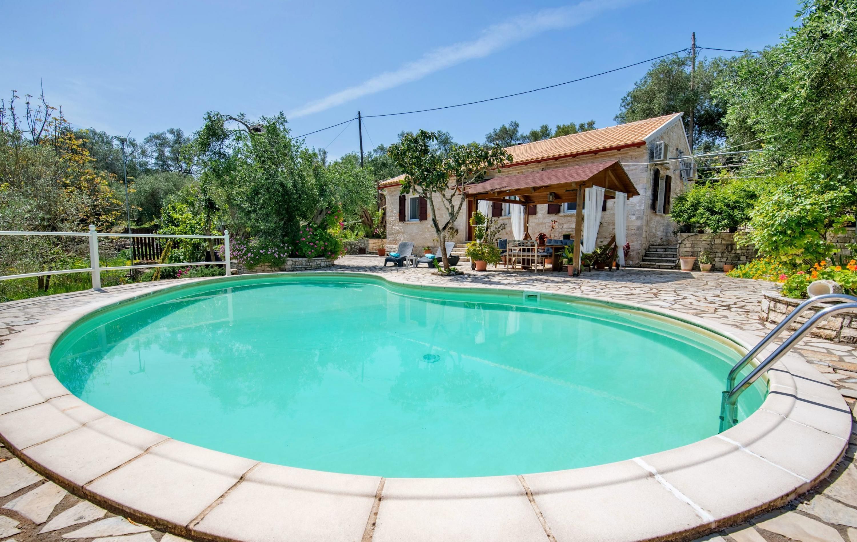 A swimming pool with a stone deck, surrounded by a house with a tiled roof and a covered patio.