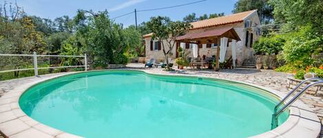A swimming pool with a stone deck, surrounded by a house with a tiled roof and a covered patio.