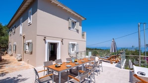 Un edificio a due piani con una terrazza, posti a sedere all'aperto e vista sul mare.