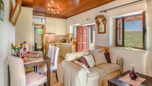 A cozy living room with a sofa, a dining table set for two, and a kitchen in the background. - Villa Melissa Paxos in Paxi (Paxos)