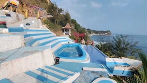 Una piscina con escalones azules que bajan a ella, rodeada de vegetación y con vistas al mar.