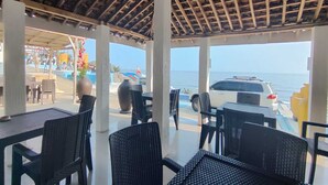 Un espacio de estar al aire libre cubierto con mesas y sillas, con vista a una playa y al mar.