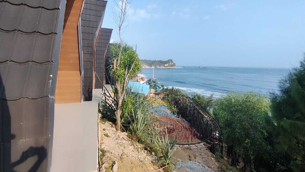 Vista costera con piscina, terraza de madera y un acantilado al fondo.