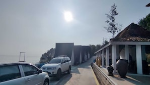 Un estacionamiento con dos autos, un edificio de techo con tejas y un muro de piedra con jarrones grandes.