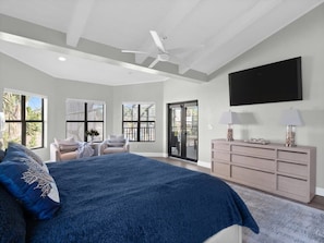 Une chambre dotée d’un grand lit, d’un ventilateur de plafond, d’un téléviseur fixé au mur et d’une porte-fenêtre coulissante donnant sur un espace extérieur.