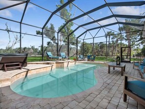 A covered outdoor swimming pool with lounge chairs and a hot tub.
