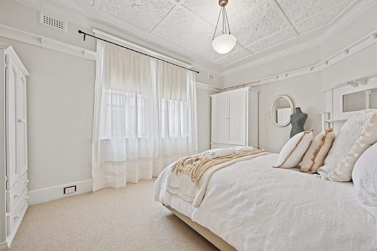 A bedroom with a large bed, a wardrobe, a mirror, and a ceiling with intricate patterns.