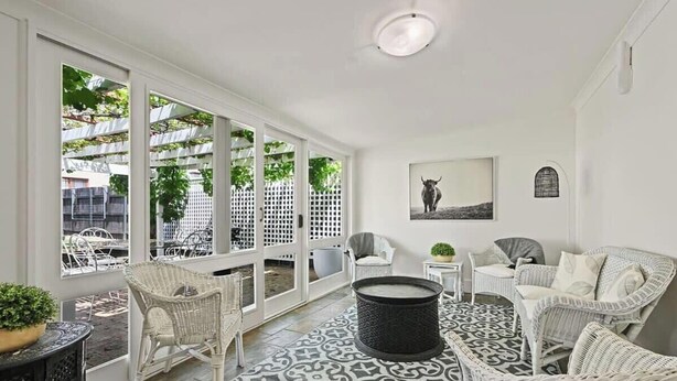 A spacious room with large windows, wicker furniture, and a patterned floor. - Hamptons House | Scandi Heritage Charm (Bathurst)