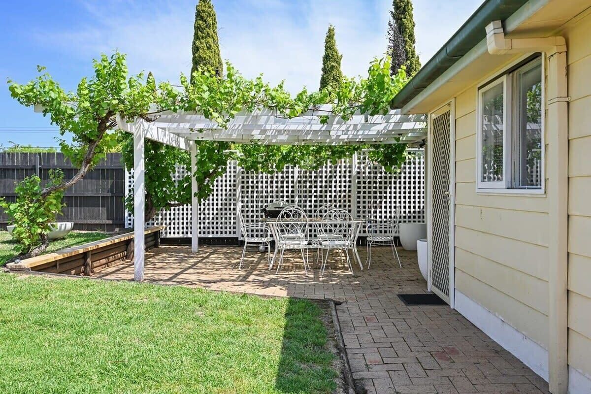 A patio with a pergola, white lattice fence, and a table with chairs.