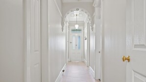 A hallway with white walls, a wooden floor, and a door at the end. - Hamptons House | Scandi Heritage Charm (Bathurst)