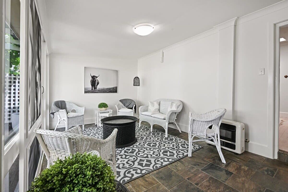 A room with white wicker furniture, a patterned rug, a black circular table, and a wall-mounted picture.