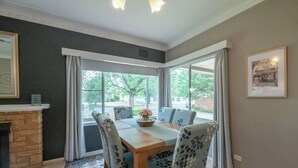 Comedor con mesa de madera, sillas, chimenea y ventanas amplias.