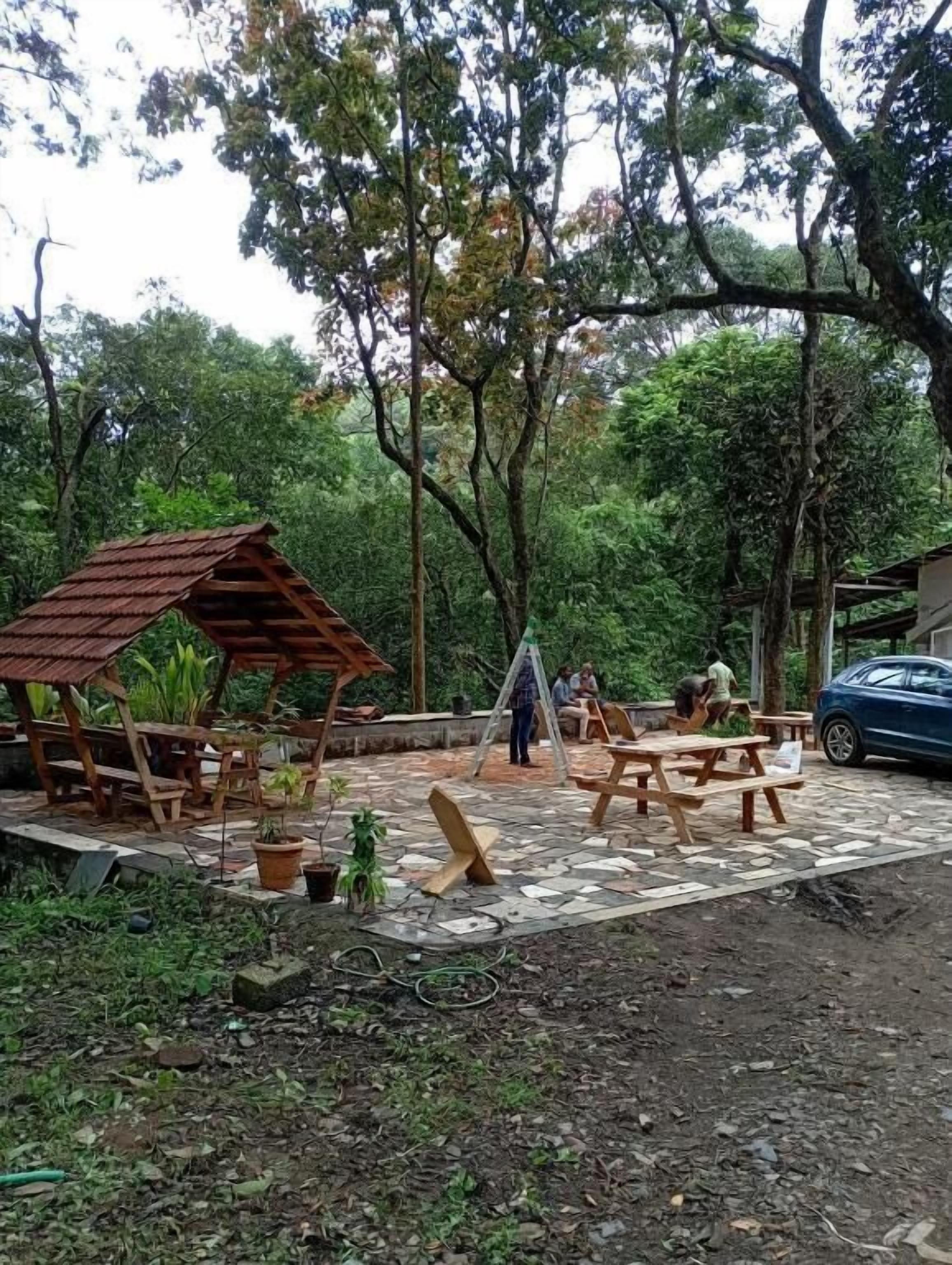 Un espacio al aire libre con mesas y bancos de picnic de madera, rodeado de árboles.