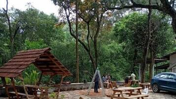 Un espacio al aire libre con mesas y bancos de picnic de madera, rodeado de árboles.