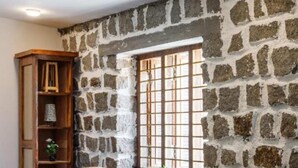 Un coin repas avec un mur en pierre, une fenêtre avec des barreaux, une table en bois, des chaises et une bibliothèque.