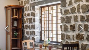 Une pièce avec un mur en pierre, une bibliothèque en bois, une fenêtre avec des barreaux et une table avec des chaises.