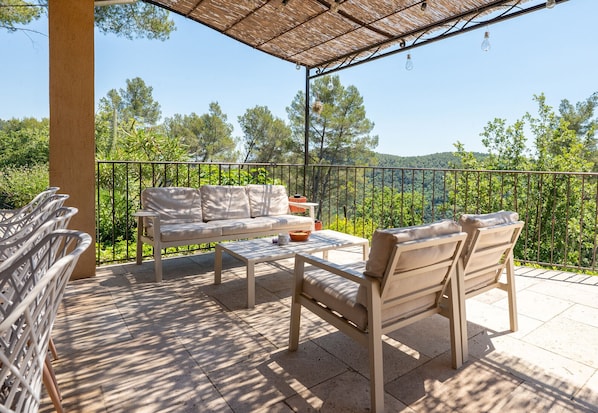 A covered outdoor seating area with a sofa, chairs, and a table, overlooking a scenic landscape. - Mas des Violettes – Luxury vacation villa in the Alpes-Maritimes (Tourretes sur Loup)