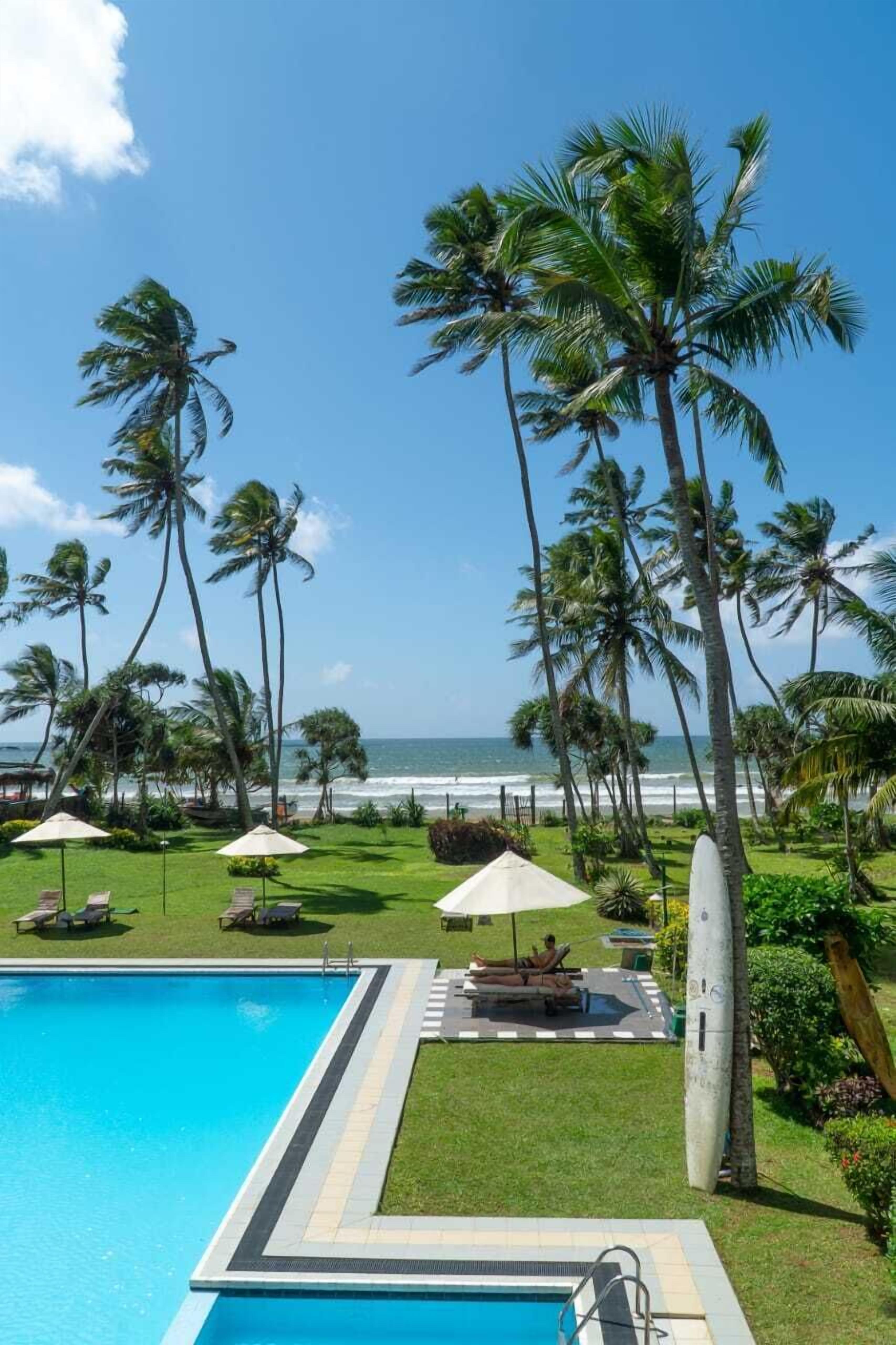A pool area with a view of the ocean, surrounded by palm trees and lounge chairs.