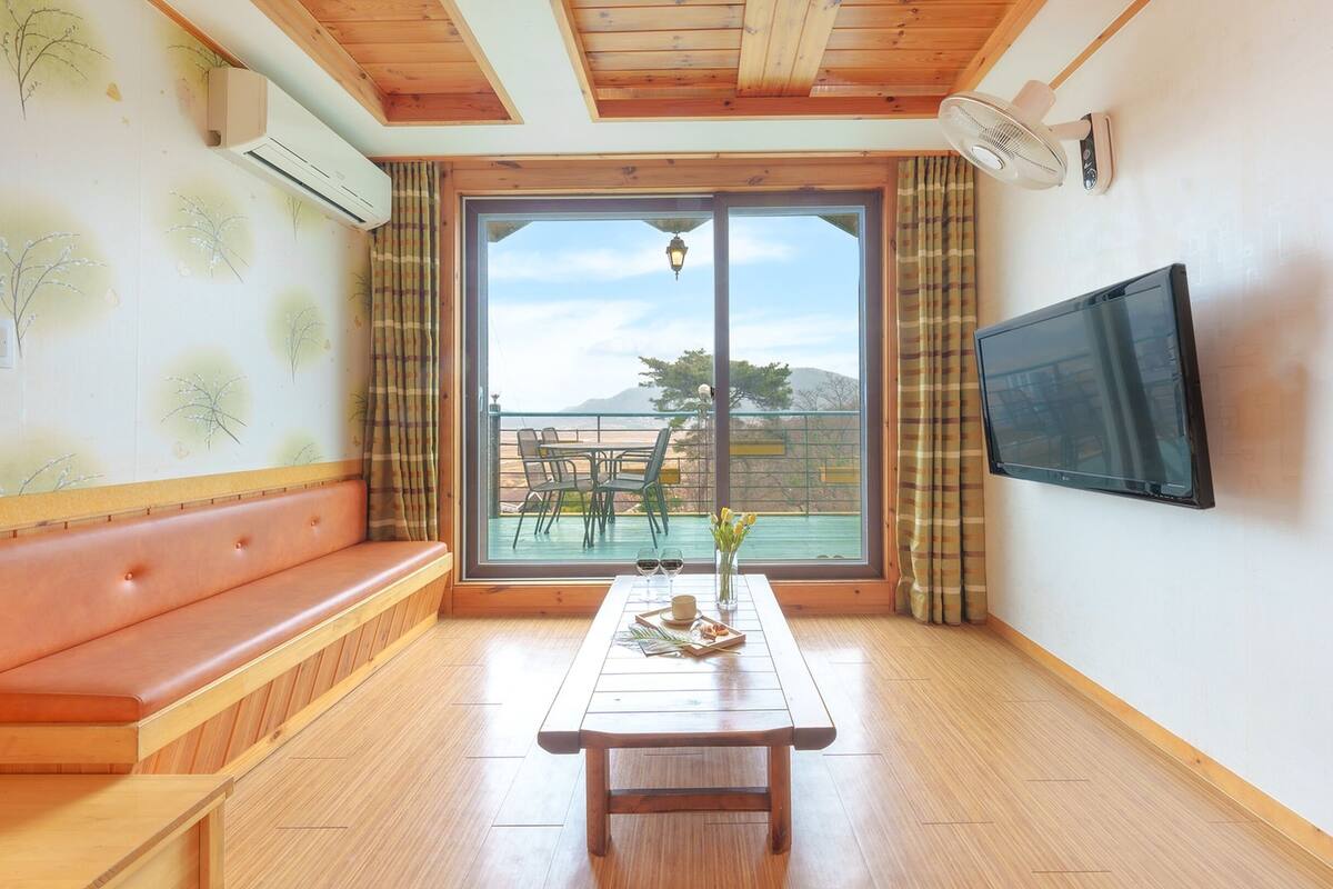 A room with a wooden bench, a table with a vase of flowers, and a TV on the wall.