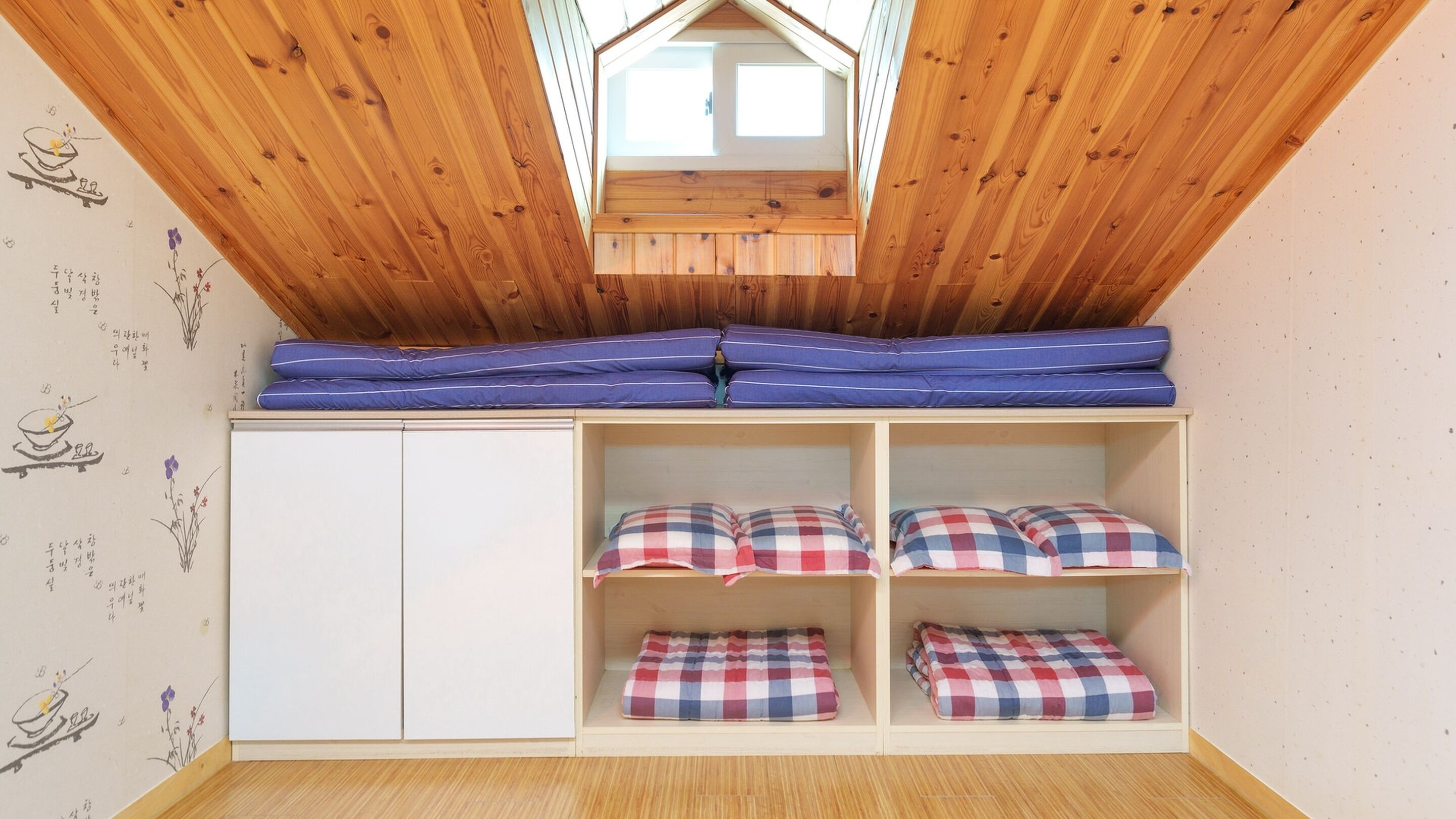 Ein Schlafsaalzimmer mit schrägem Dach, einem Oberlicht und einem Etagenbett mit blauer Bettwäsche.
