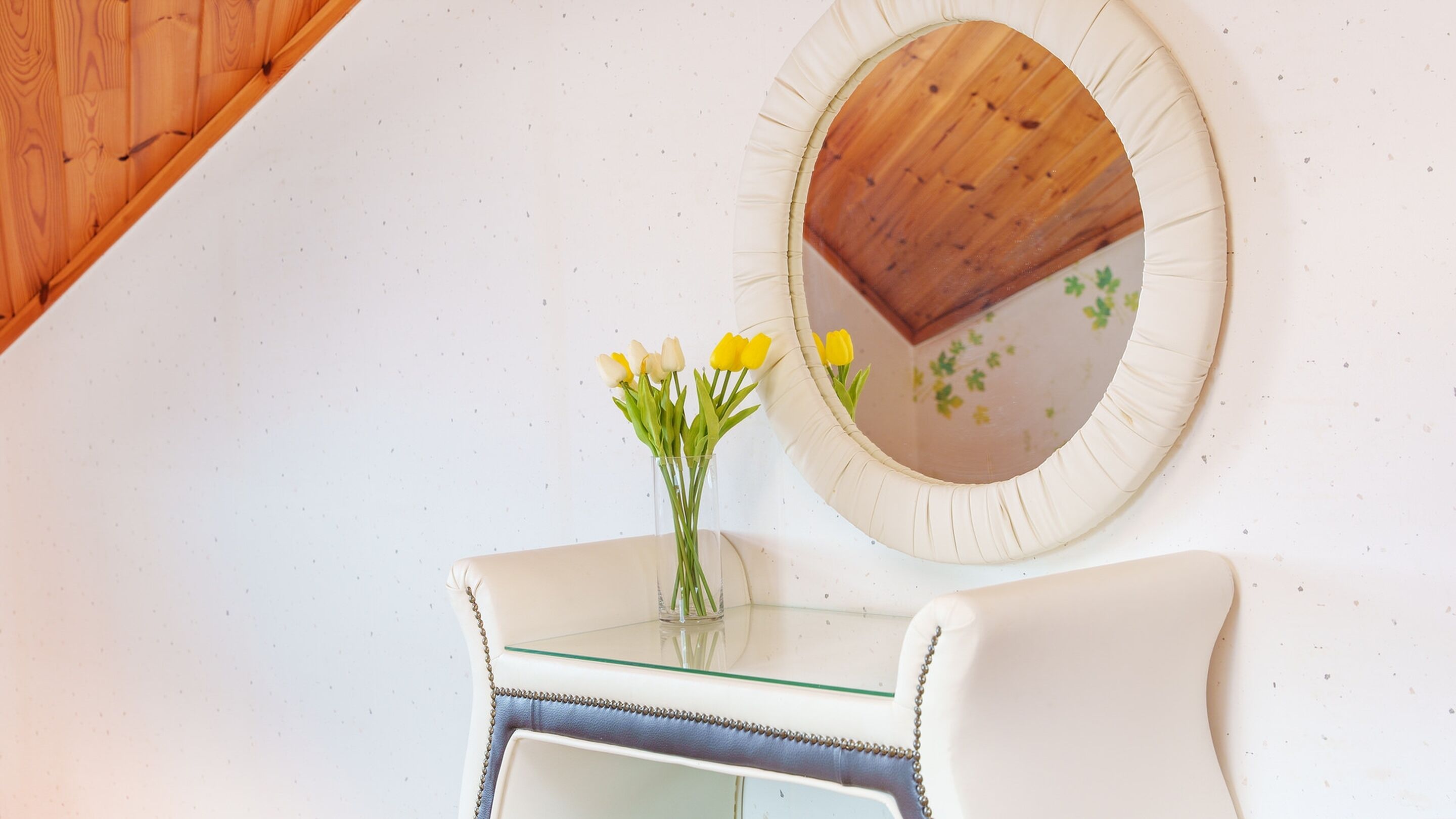 A white chair and a glass table with a vase of yellow flowers.