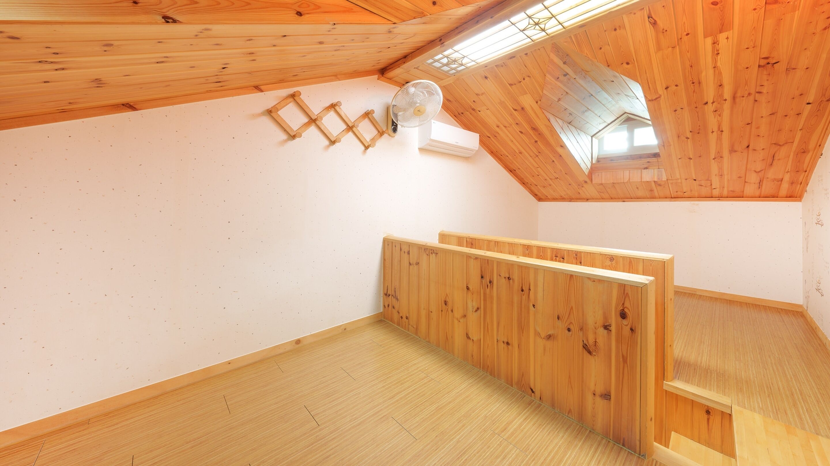 A room with a sloped ceiling, wooden walls, a white air conditioning unit, and a fan mounted on the wall.