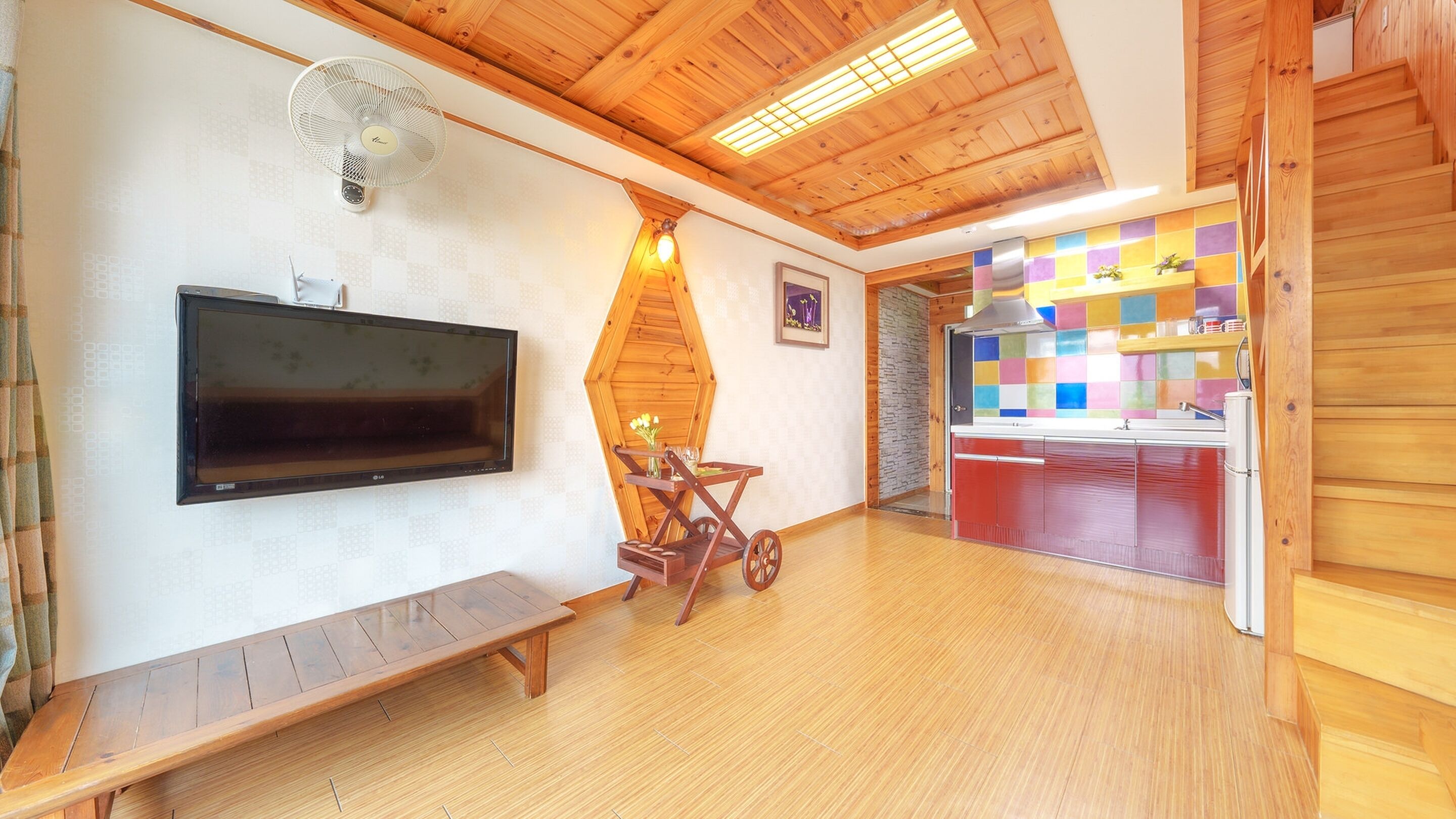 Un interior de madera con un televisor de pantalla plana, un banco, un ventilador y un colorido salpicadero de azulejos.