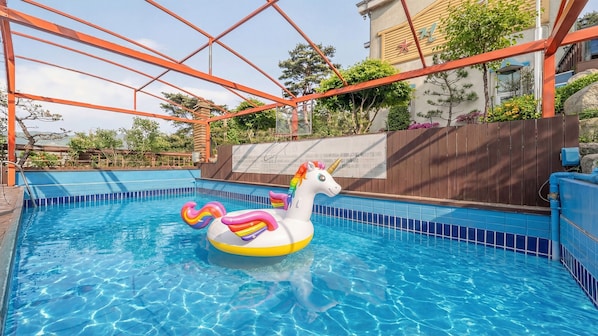 Una piscina con un flotador de unicornio, rodeada por una valla de madera y árboles.