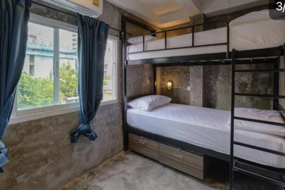 Quarto com beliche, janela, cortinas e luminária fixada na parede.