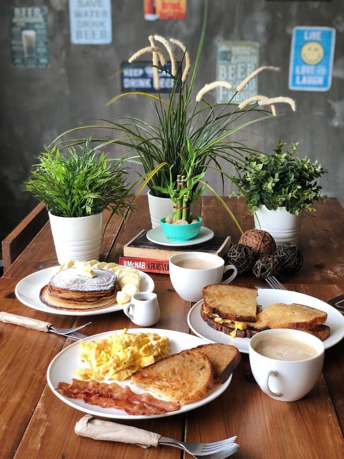Ein Frühstückstisch mit Pfannkuchen, Eiern, Toast und Kaffee, umgeben von Blumentöpfen.