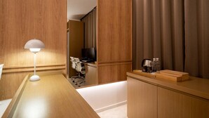 Ein Hotelzimmer mit Schreibtisch aus Holz, einer Lampe, einem Fernseher und einer Minibar.