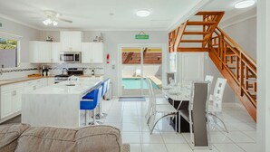 Et moderne køkken med hvide skabe, en central ø og et spiseområde med udsigt til en pool.