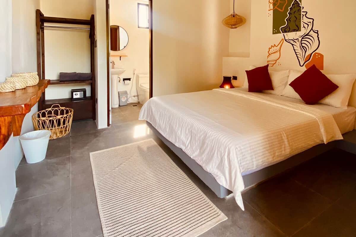 A modern bedroom with a bed, a ceiling fan, a wall-mounted air conditioner, a woven basket, and a small desk with a chair.