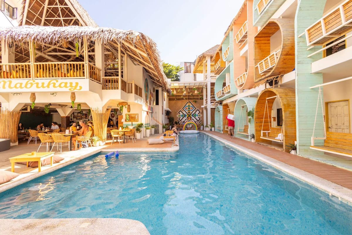 A pool area with a restaurant named 'Mabu Kay' on the left, surrounded by buildings with unique architecture.