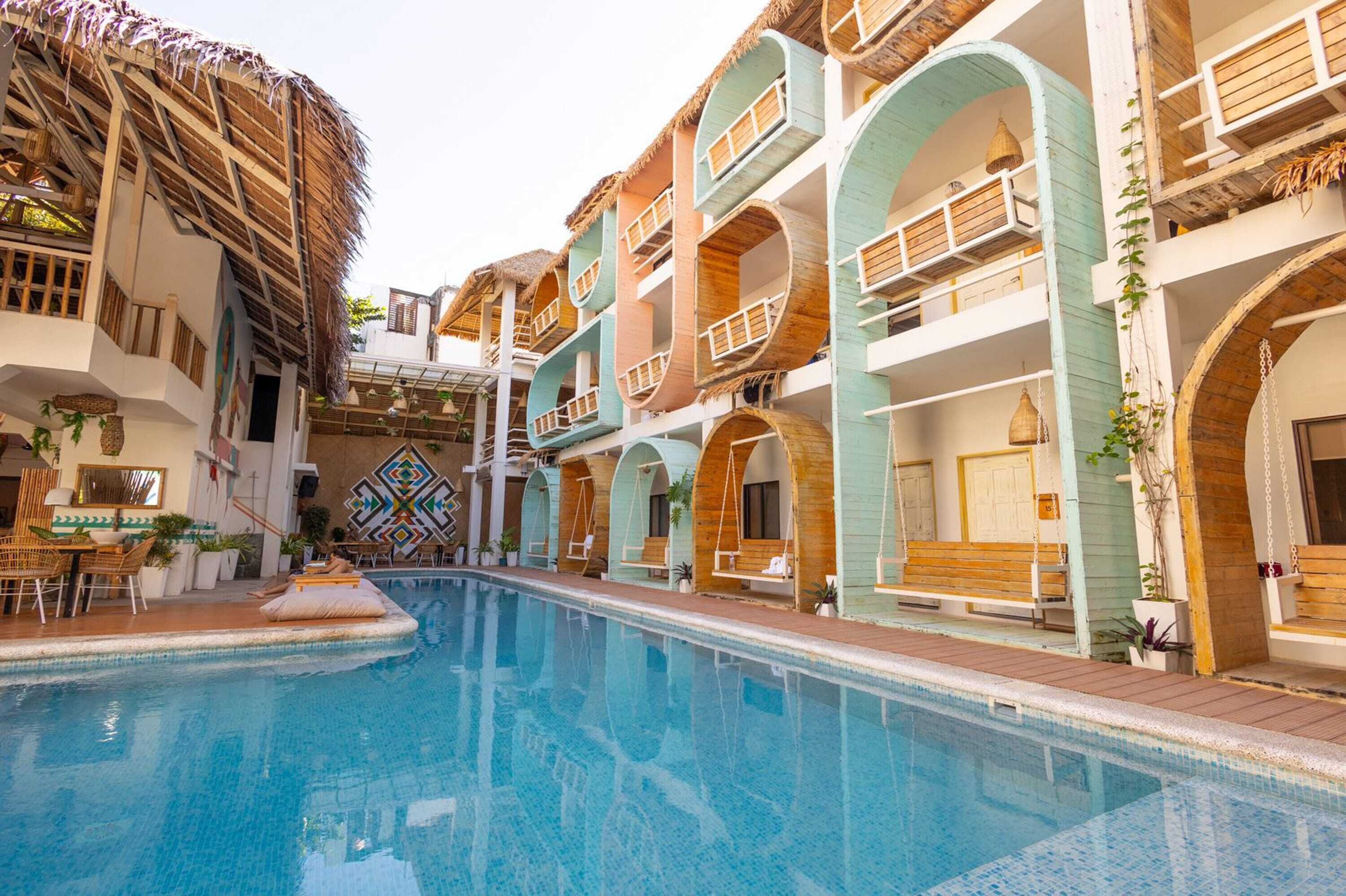 A swimming pool with a thatched roof structure, multi-level wooden balconies, and a central staircase.
