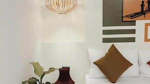 A bedroom with a bed, a hanging light fixture, a wall-mounted painting, and a potted plant.